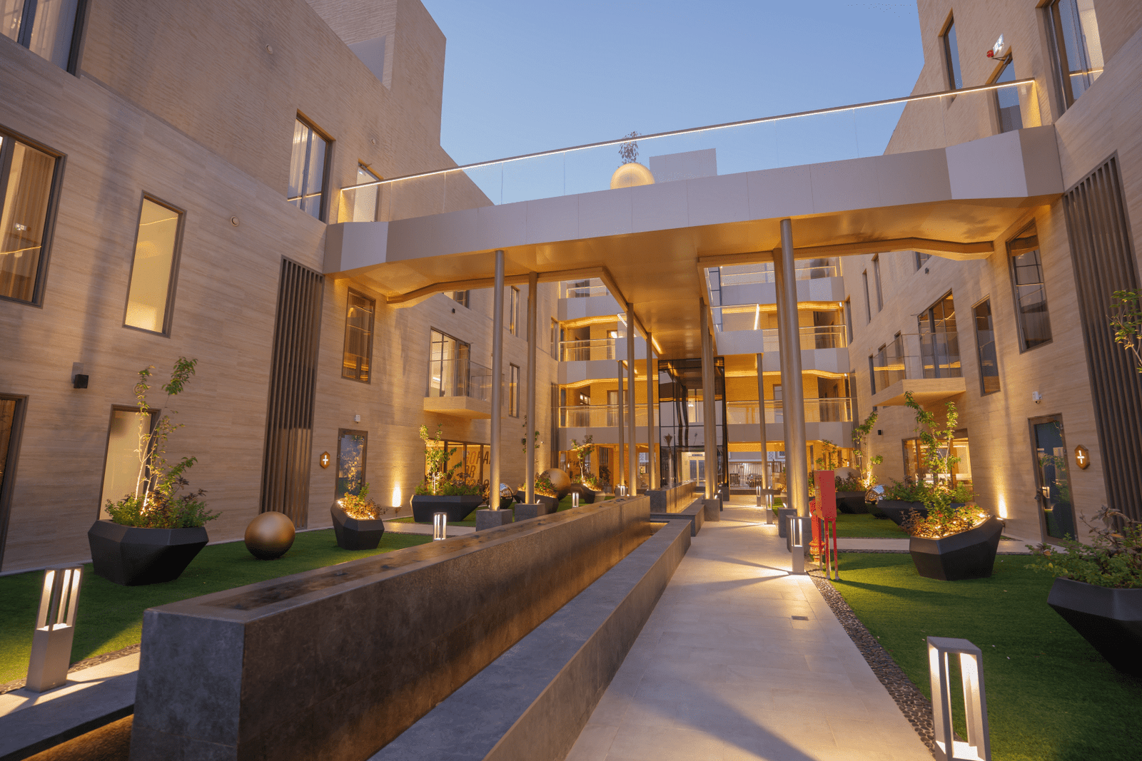 Landscaped walkway with planters, bridge, and ambient lighting.